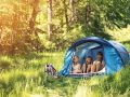 Little girl and brothers are camping in a tent in a sunny forest. Kids aged 5 and 9 are smiling happiliy sitting inside of blue tent. Sunny summer day. Slightly soft.