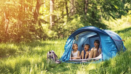 Little girl and brothers are camping in a tent in a sunny forest. Kids aged 5 and 9 are smiling happiliy sitting inside of blue tent. Sunny summer day. Slightly soft.